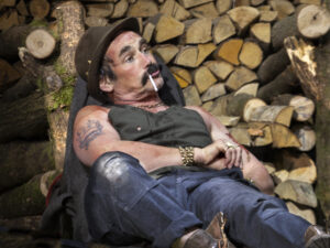 Actor Mark Rylance sits against a pile of logs in a scene from Jerusalem by Jez Butterworth