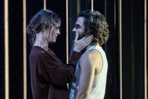Production shot from Phaedra at the National Theatre in London February 2023 showing Mckenzie Davis holding Assaad Bouab's face and staring into his eyes