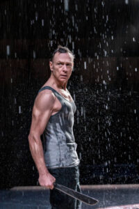 Production photo from Medea at sohoplace theatre in London February 2023 showing a man in a vest in the rain
