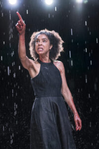 Production photo from Medea at sohoplace theatre in London February 2023 showing a woman holding up her hand in the rain