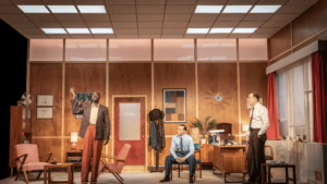 Set depicting a 1950s office with three actors in Retrograde at the Kiln Theatre