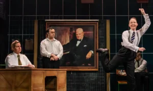 Two actors watch as another dances in front of a painting of Winston Churchill in the stage musical Operation Mincemeat at the Fortune Theatre June 2023
