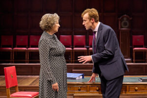 John Heffernan, a male actor, stands in front of Deborah Findlay, a female actor, and leans forward to make a point, in the play The Inquiry at Chichestre's Minerva Theatre