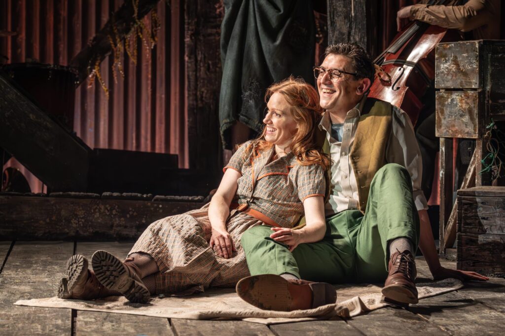 Two actors Clare Foster and John Dalgliesh sit together smiling in a scne from The Curious Case of Benjamin Button The Musical